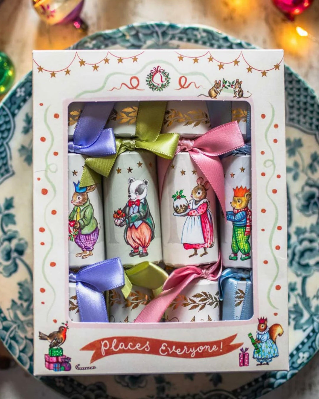 Set of mini Christmas crackers with cartoon animals and colourful bows in a decorative box on a patterned surface.