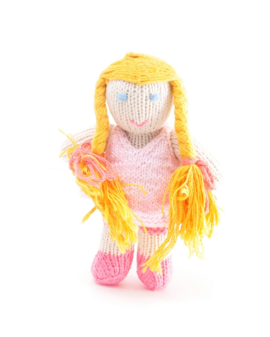 A handmade knitted doll with long yellow yarn hair, a pink dress, and pink shoes, standing against a plain white background.