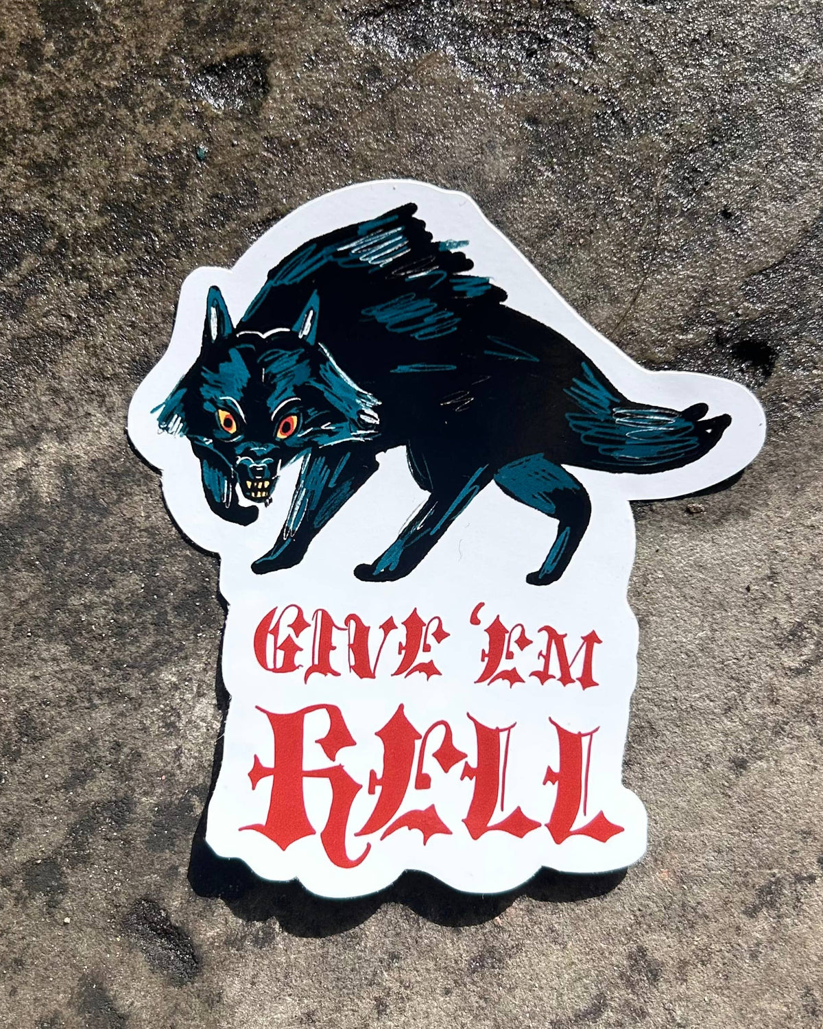 A die-cut vinyl sticker featuring a black and teal werewolf with glowing red eyes above the gothic red text 'GIVE 'EM HELL', shown on a textured gray concrete surface.